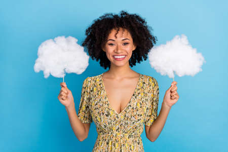 Photo of adorable sweet woman wear print dress holding two white fluffy clouds isolated blue color backgroundの写真素材