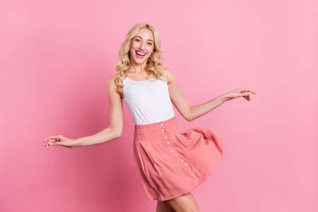 Portrait of feminine thin attractive cheerful blond girl dancing isolated over pink pastel color backgroundの写真素材