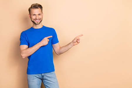 Photo of young cheerful guy indicate fingers empty space direct banner suggest isolated over beige...