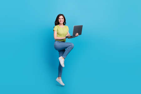 Full size photo of sweet millennial brunette lady jump hold laptop wear t-shirt jeans sneakers...