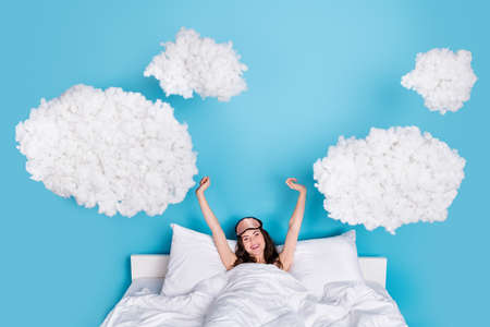 Portrait of attractive cheerful healthy girl waking up stretching in cosy bed isolated over bright...