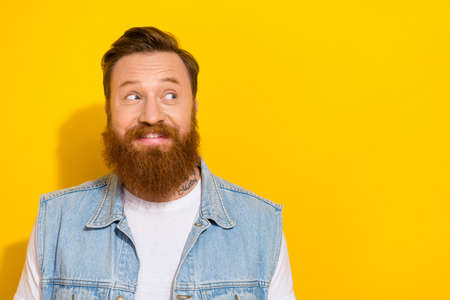 Photo of funny dreamy guy dressed denim vest smiling looking empty space isolated yellow color backgroundの写真素材