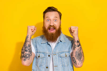 Photo of lucky excited guy dressed denim vest smiling rising fists isolated yellow color backgroundの写真素材