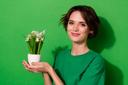 Photo of charming adorable young lady dressed casual t-shirt holding office plant isolated green color backgroundの写真素材