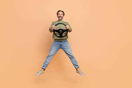 Full size portrait of satisfied excited man hold wheel have good mood isolated on beige color...