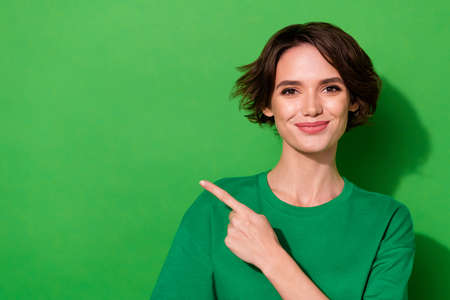 Photo of shiny cute woman wear casual t-shirt pointing finger empty space isolated green color...