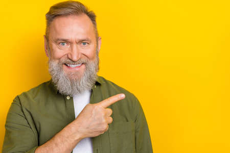 Portrait of positive friendly person beaming smile direct finger empty space isolated on yellow color backgroundの写真素材