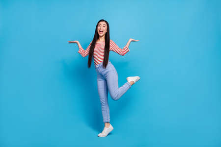 Full length photo of pretty excited woman wear striped shirt dancing comparing arms empty space...