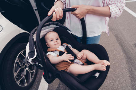 Cropped portrait of mother hands hold toddler sitting safety chair street outside car salon