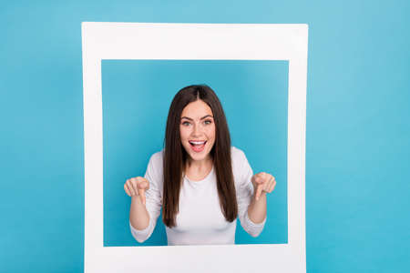 Portrait of charming excited lady in white frame point fingers down follow subscribe isolated on...