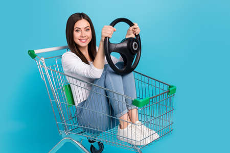 Photo of funny cheerful girl sitting in pushcart hold steering wheel practice to ride card isolated...