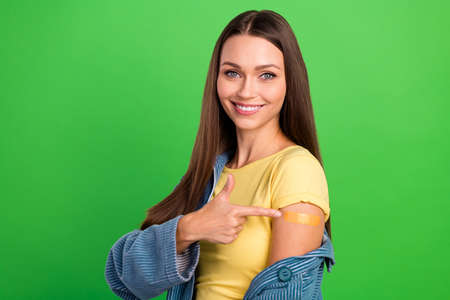 Photo of pretty cheerful person finger indicate shoulder vaccine patch isolated on green color...