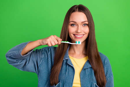 Portrait of positive pretty person arm hold toothbrush toothy smile isolated on green color backgroundの写真素材