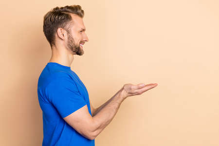 Profile side photo of young man hold arms demonstrate promotion offer look empty space isolated over...