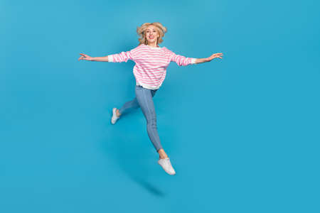Photo of adorable pretty woman wear striped sweater jumping high running arms sides isolated blue...