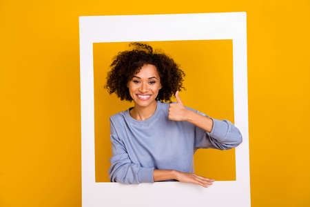 Photo of cheerful pretty person hand finger demonstrate thumb up through paper window isolated on yellow color backgroundの写真素材