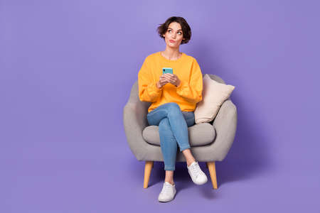 Portrait of attractive minded girl sitting using gadget chatting creating post smm isolated over violet lilac color backgroundの写真素材