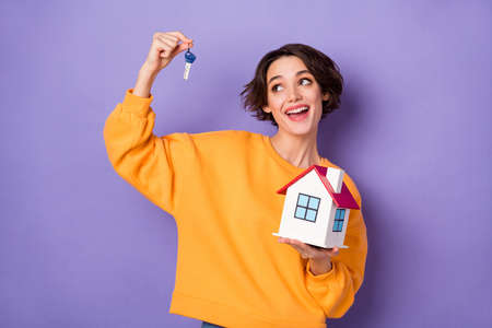 Portrait of attractive cheerful girl holding small home on palm keys new property isolated over violet lilac color backgroundの写真素材