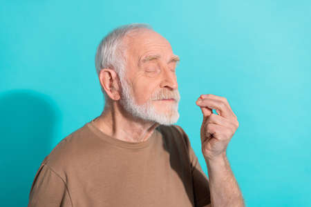 Portrait of attractive cheery dreamy grey-haired man pretending tasting good food isolated over bright blue color backgroundの写真素材