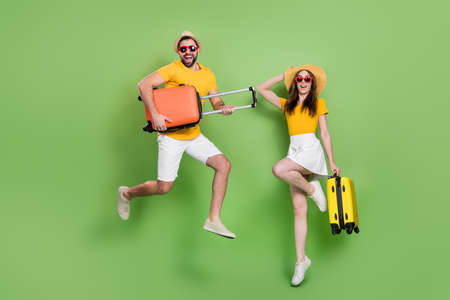 Full size photo of two excited energetic people jumping hold suitcase isolated on green color...