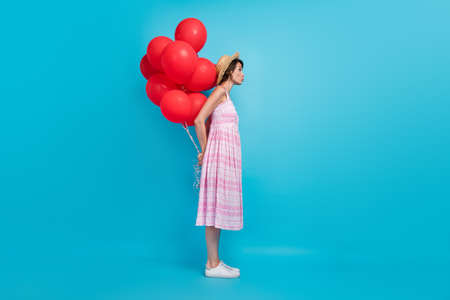 Full size photo of flirty millennial lady hold balloons blow kiss wear hat long sarafan sneakers isolated on blue backgroundの写真素材