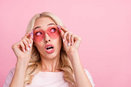 Photo of curious millennial blond lady look empty space wear spectacles t-shirt isolated on pink color backgroundの写真素材