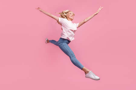 Full length photo of cool young blond lady jump wear t-shirt jeans sneakers isolated on pink backgroundの写真素材