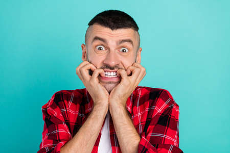 Photo of scared young brunet guy bite hands wear red shirt isolated on teal color backgroundの写真素材