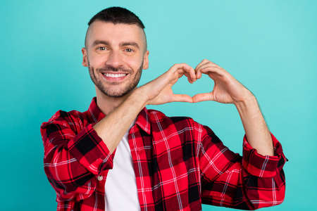Photo of cheerful positive young man show fingers small heart shape isolated on teal color backgroundの写真素材