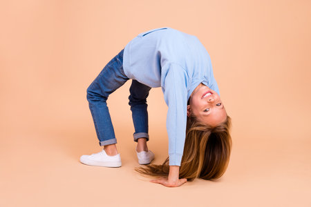 Full size photo of funny cute pupil practice acrobatics standing bridge isolated on beige color backgroundの写真素材