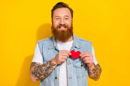 Photo of candid satisfied man hold small paper heart postcard toothy smile isolated on yellow color...