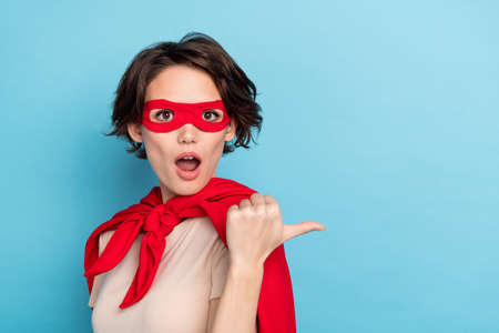Photo of impressed shocked lady dressed red mantle pointing thumb back empty space isolated blue color backgroundの写真素材