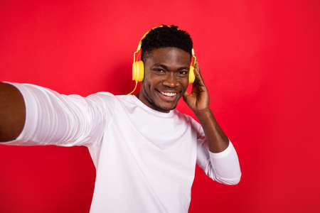 Photo of positive funky person hand touch headphones make selfie isolated on red color backgroundの写真素材