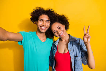 Photo of happy charming young dark skin couple make selfie v-sign smile isolated on yellow color...