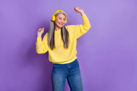 Photo of sweet shiny retired woman wear sweater earphones dancing isolated violet color backgroundの写真素材