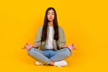 Full body photo of focused pretty person sit floor arms fingers meditate isolated on yellow color backgroundの写真素材