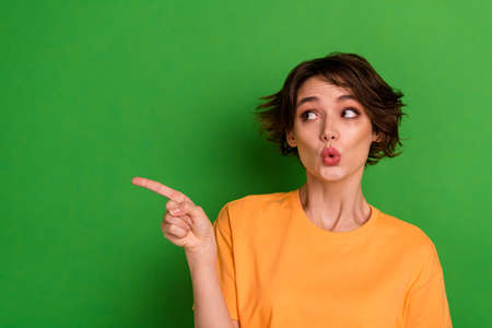 Photo of pretty shocked young woman dressed orange t-shirt looking pointing empty space isolated green color backgroundの写真素材