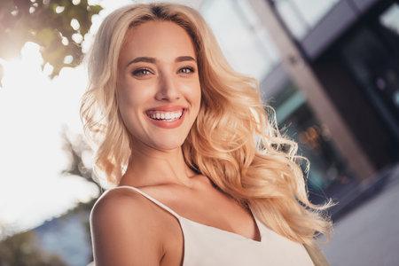 Portrait of attractive cheerful wavy haired girl visiting center strolling enjoying warm sun shine evening in town outdoorsの写真素材