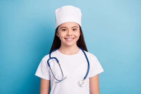 Photo portrait of little girl in medical uniform headwear smiling with stethoscope isolated on bright blue color backgroundの写真素材