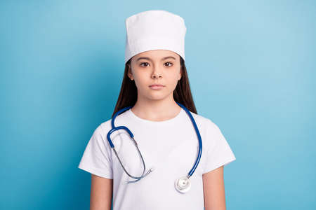 Photo portrait of little girl serious in medical uniform headwear isolated on bright blue color backgroundの写真素材