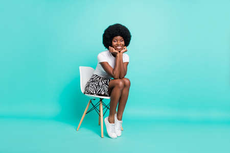 Photo of shiny adorable dark skin lady wear casual clothes smiling sitting chair arms cheeks cheekbones isolated teal color backgroundの写真素材