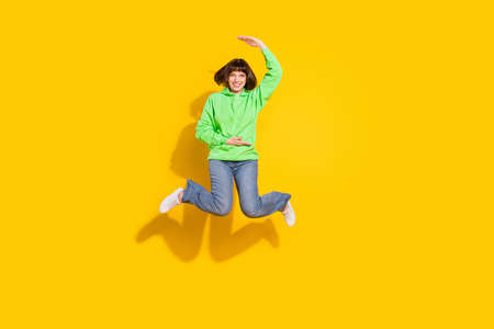 Full size photo of happy pretty lovely lady jump up hold hand measure empty space isolated on yellow...