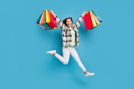 Full size photo of young excited girl happy positive smile jump hold shopping bags isolated over blue color backgroundの写真素材