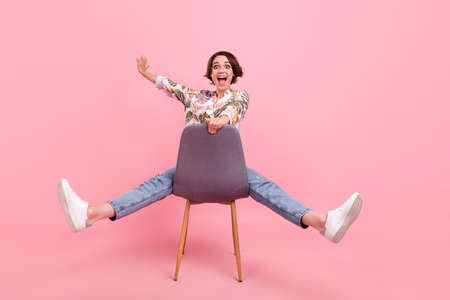 Full length body size photo woman riding on chair laughing childish crazy isolated pastel pink color backgroundの写真素材