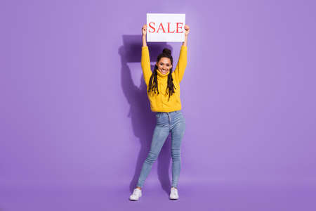 Full size photo of optimistic nice brunette girl show banner wear sweater jeans isolated on purple backgroundの写真素材