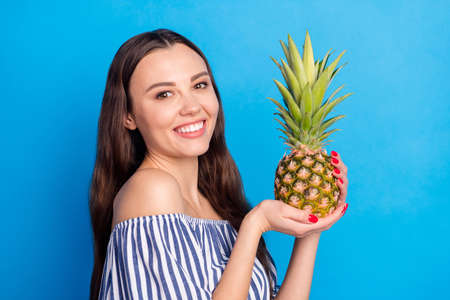 Photo of shiny adorable young lady wear off-shoulders clothes holding pineapple smiling isolated blue color backgroundの写真素材