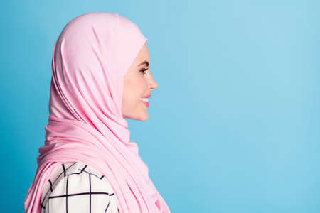 Close-up profile side view portrait of pretty cheerful content muslimah girl copy space isolated over bright blue color backgroundの写真素材