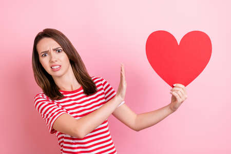 Photo of young woman unhappy dislike refuse hold red paper heart decline isolated over pink color...