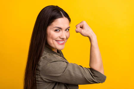 Profile side photo of happy nice positive young woman raise fist flex muscle isolated on yellow color backgroundの写真素材