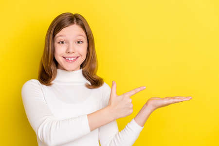 Photo of young girl happy positive smile point finger product promo offer suggest isolated over yellow color backgroundの写真素材